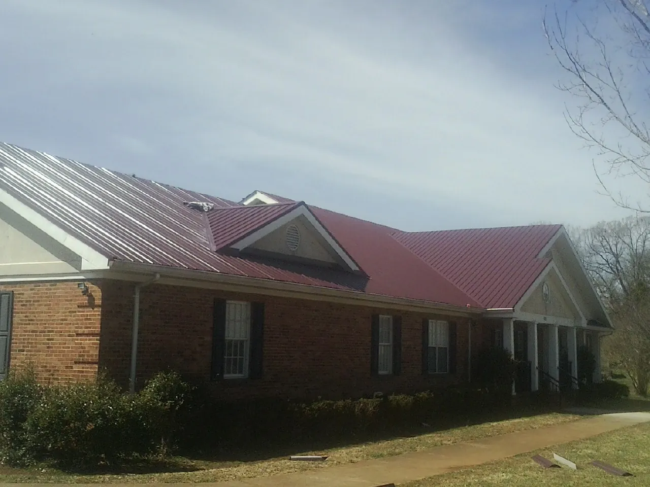 Red metal roof with gabled entries on a long brick building, from a Hail Damage Roof Repair job in Wyandotte