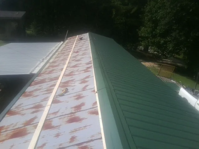 Old rusted panels beside newly installed green metal roofing — Wind Damage Roof Repair by Roofing Brothers in Wyandotte