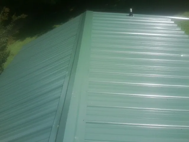 New green metal panels meeting at the ridge of a roof — Flat Roof Repair work by our crew in Wyandotte