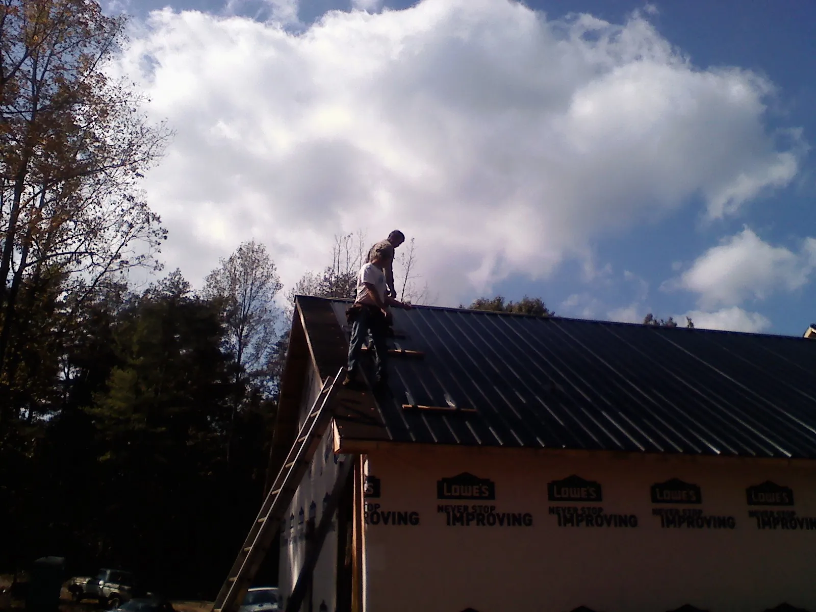 Roofer fastening dark metal panels high against a cloudy sky, from a Roof Inspection job in Wyandotte