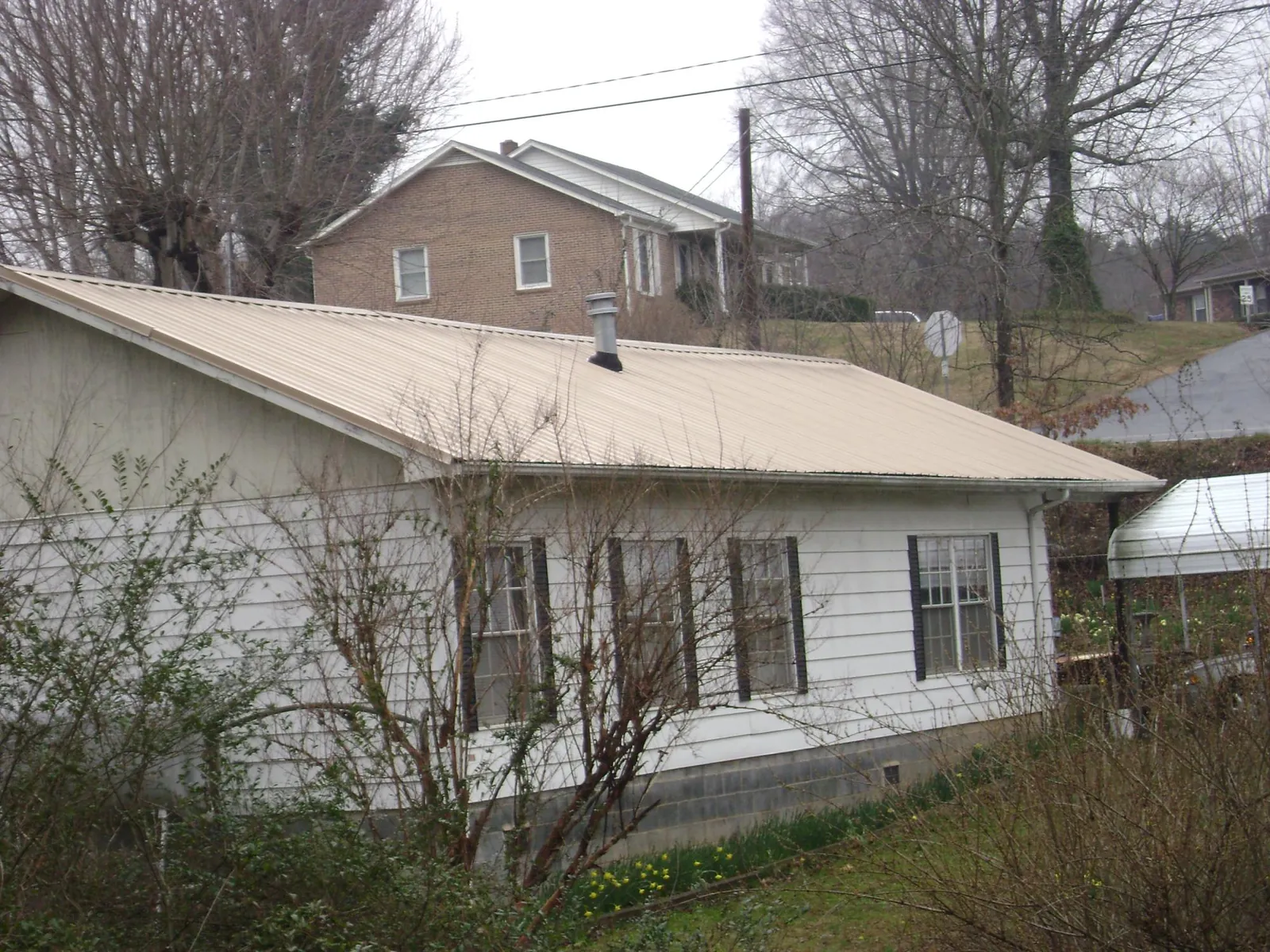 Tan metal roof on a white sided house set into a hillside — Commercial Roofing by Roofing Brothers in Wyandotte