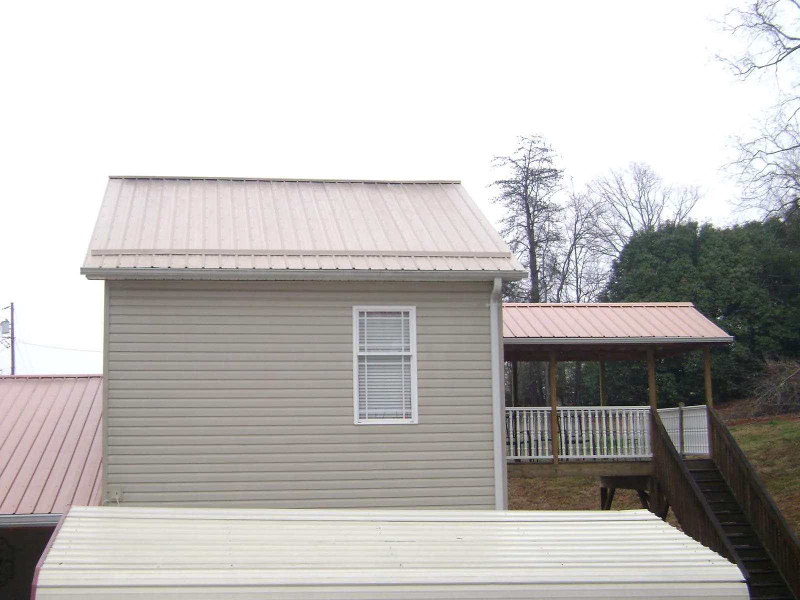 Tan metal roofs on a two story addition and attached porch, from a Roof Replacement job in Wyandotte